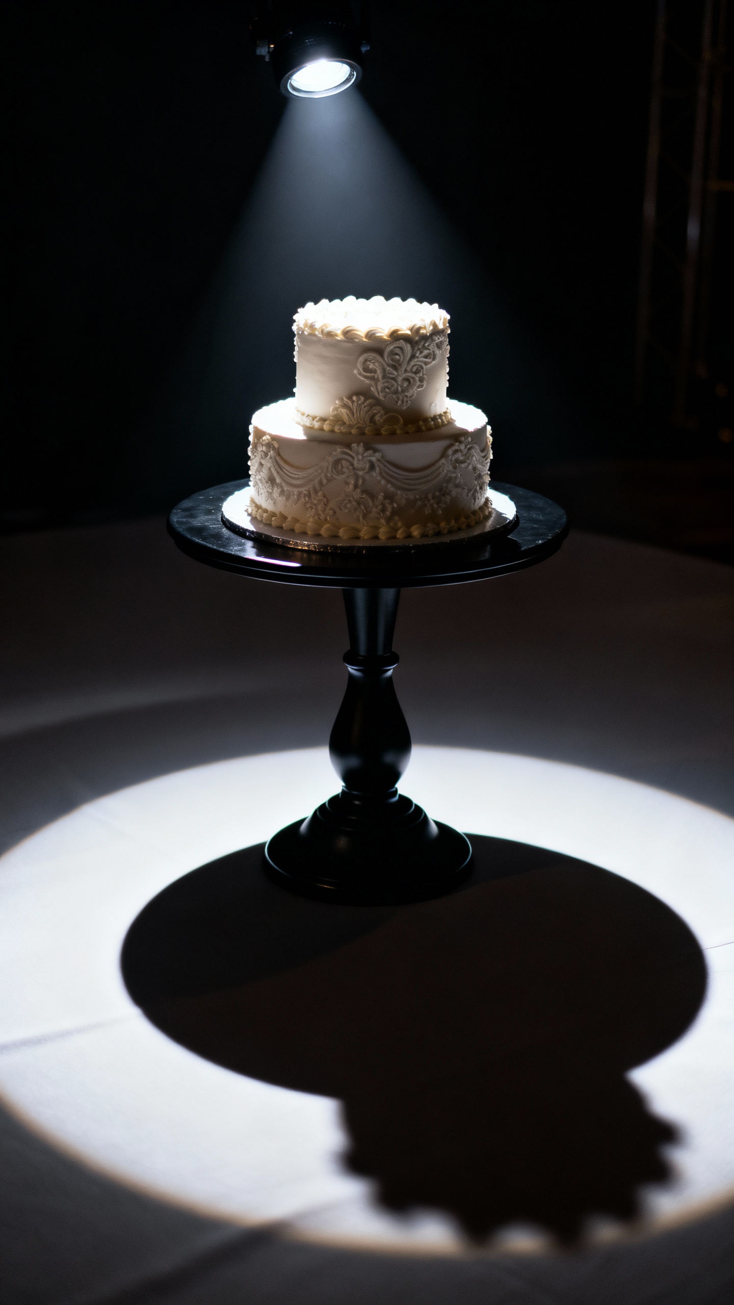 Pinspotted wedding cake on matte black stand, dramatic shadows