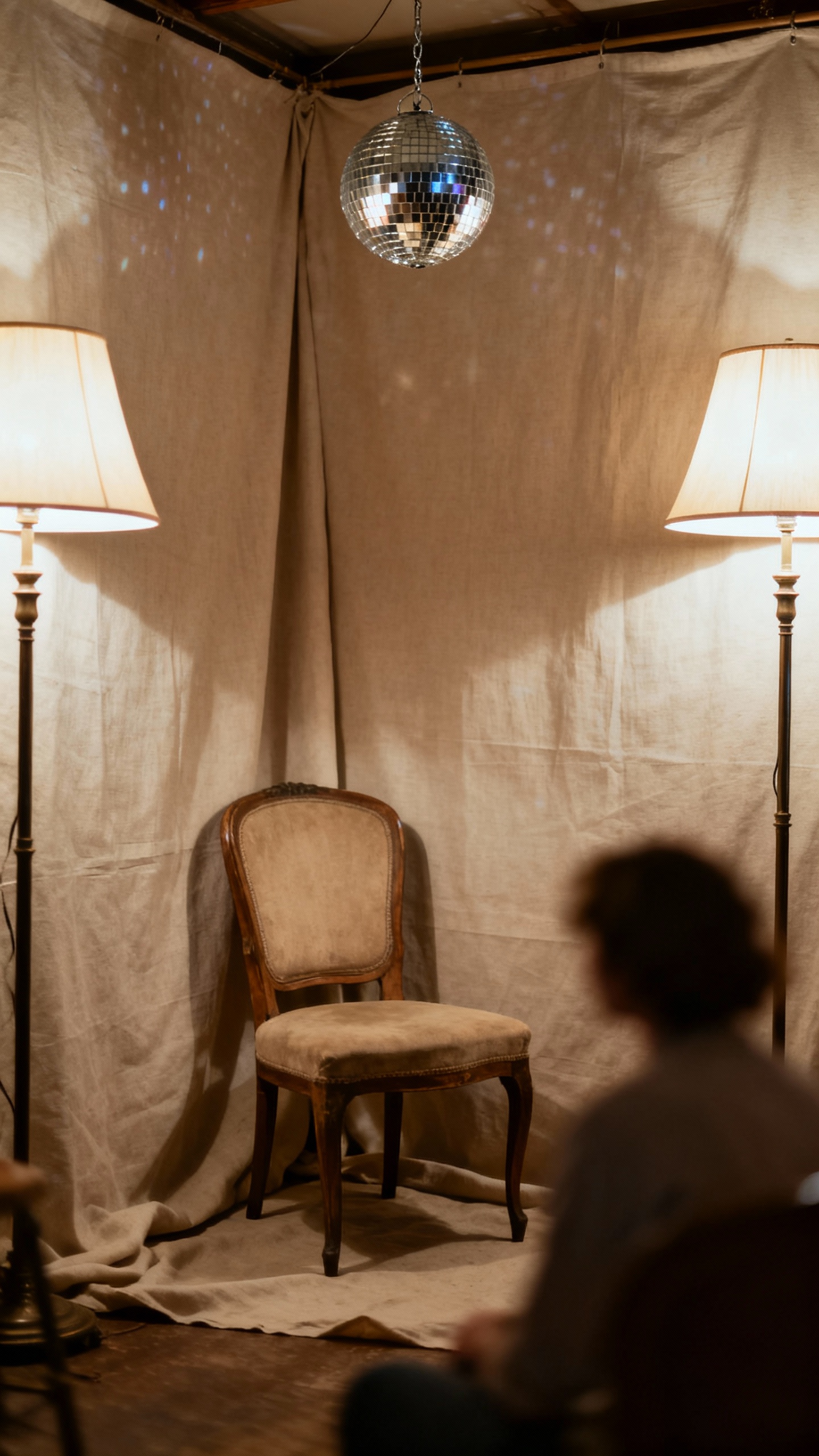 Soft-lit photo corner with neutral fabric backdrop, vintage chair, single disco ball, side lamps, sh