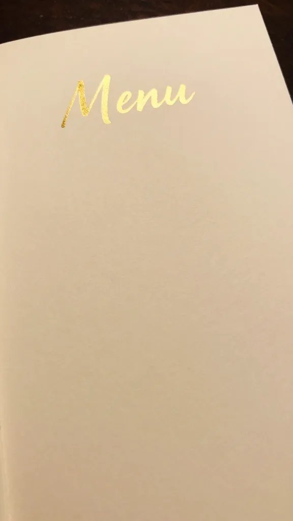 closeup of a handwritten menu card with gold foil on cream paper